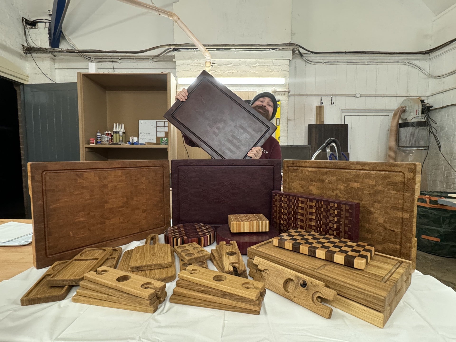A maker in the workshop displaying a wooden board, surrounded by crafted pieces